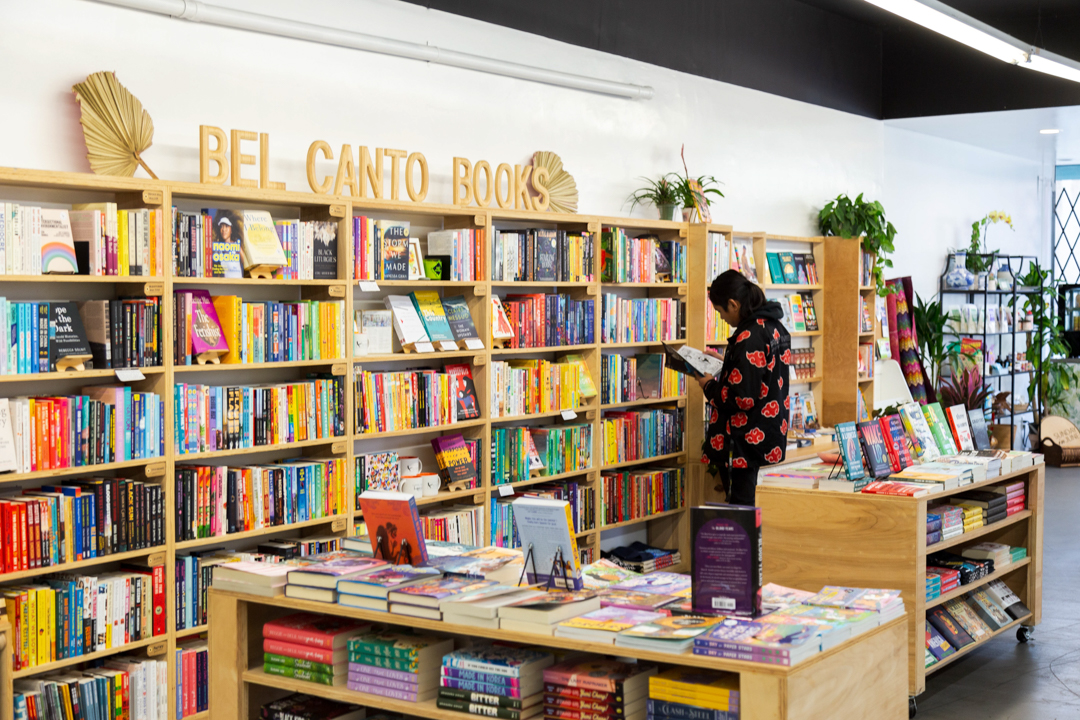 The interior of KUBO LB, Long Beach filled with book shelves and book counters, with one person shopping.