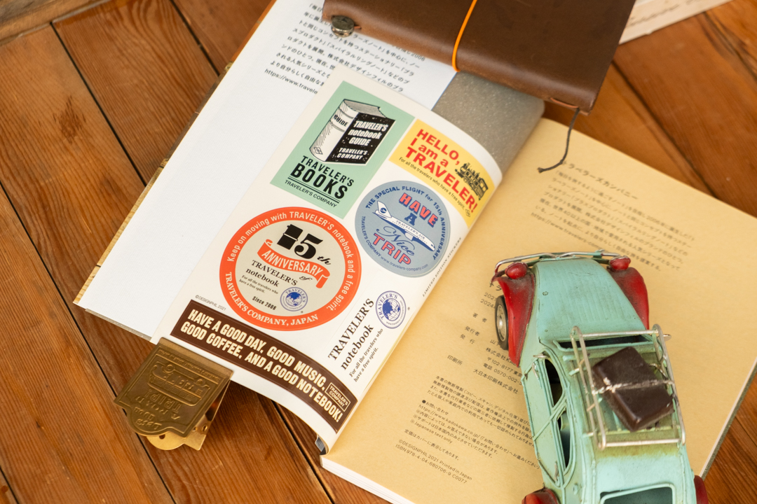 The TRAVELER'S GUIDE book propped open with a brass clip, a TRAVELER'S notebook beside a toy car on a wooden table. 