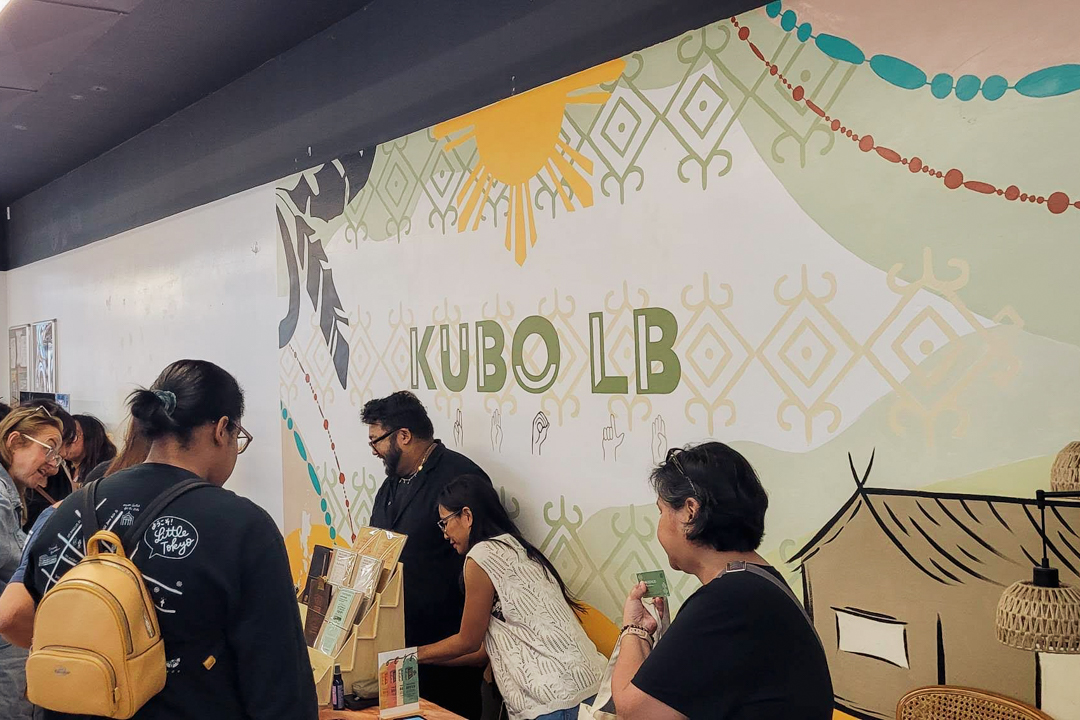 People browse the TRC USA booth at KUBO LB, featuring books, paper goods and stationery on the vendor table. The atmosphere is lively and engaging.