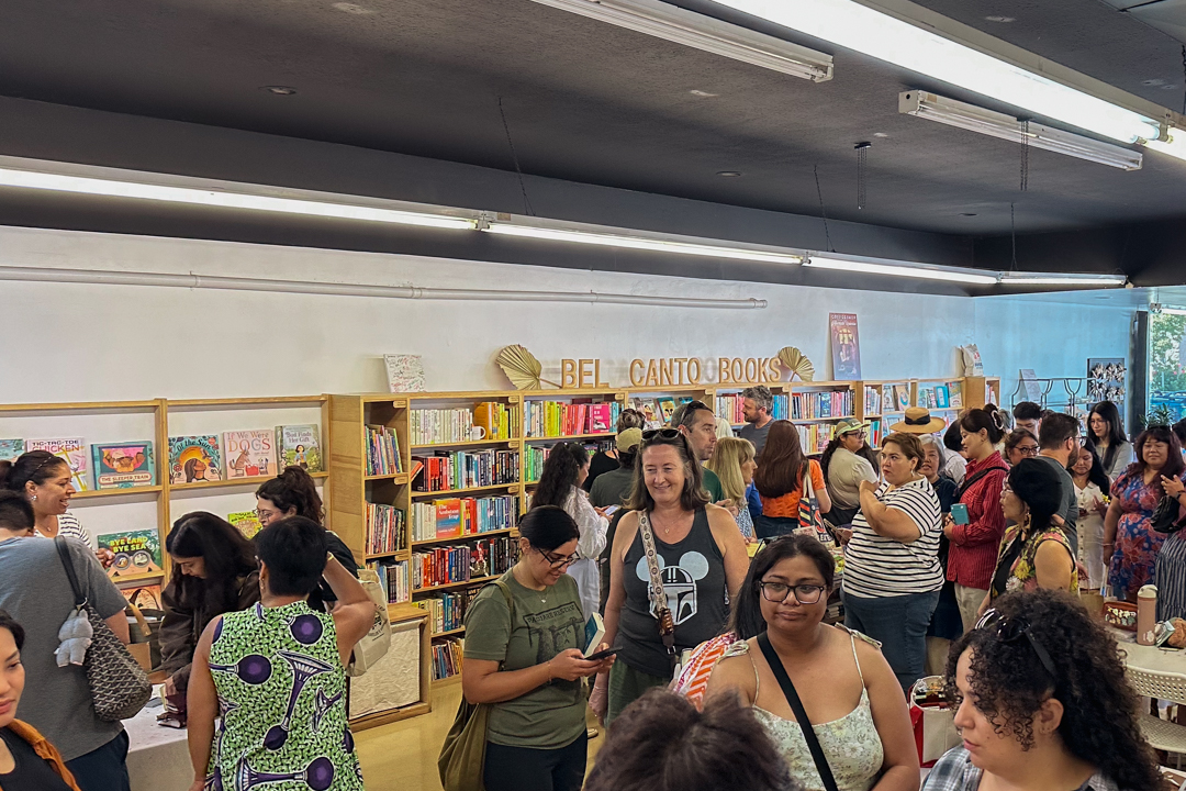 A bustling bookstore TRC USA pop-up event at "Bel Canto Books" with diverse individuals chatting and browsing shelves filled with colorful books. The atmosphere is lively and inviting.