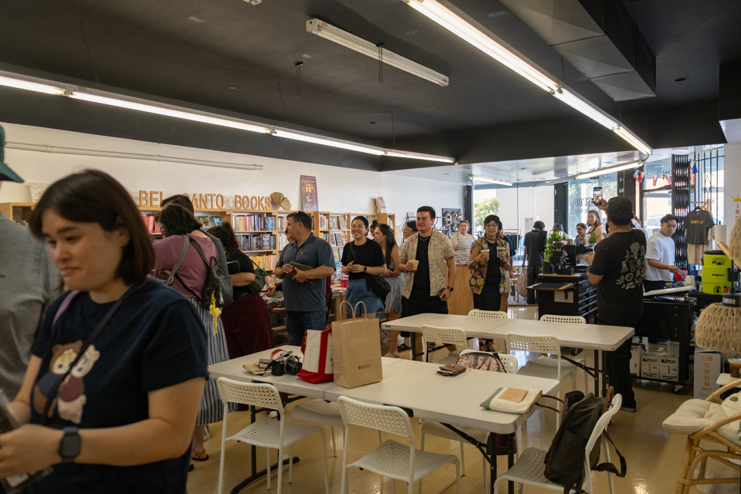 A bustling bookstore TRC USA pop-up event at "Bel Canto Books" with diverse individuals chatting and browsing shelves filled with colorful books. The atmosphere is lively and inviting.