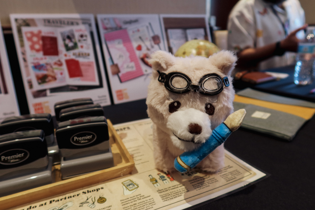 The TRC Stamp Caravan stamps beside a plush doll of a dog holding a fountain pen at the TRC USA table at the SF Pen Show.