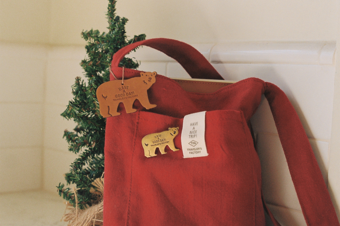 TF Holiday bear tag and brass badge on a red sacoche.