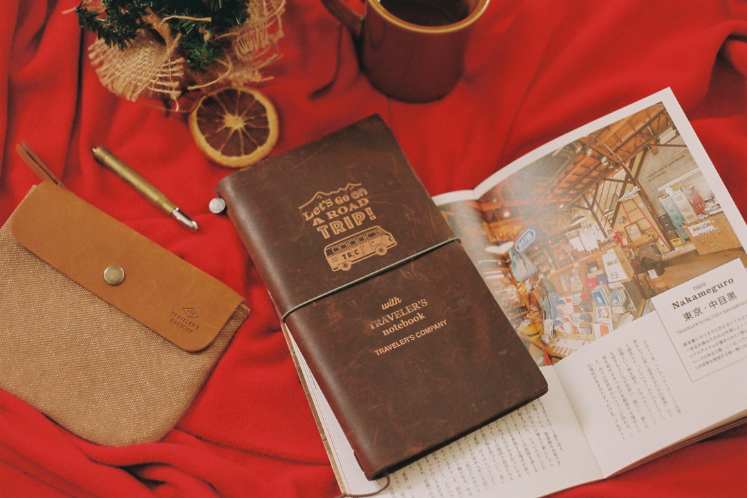 A TRAVELER'S notebook ROAD TRIP next to an open book and a TF canvas pouch.