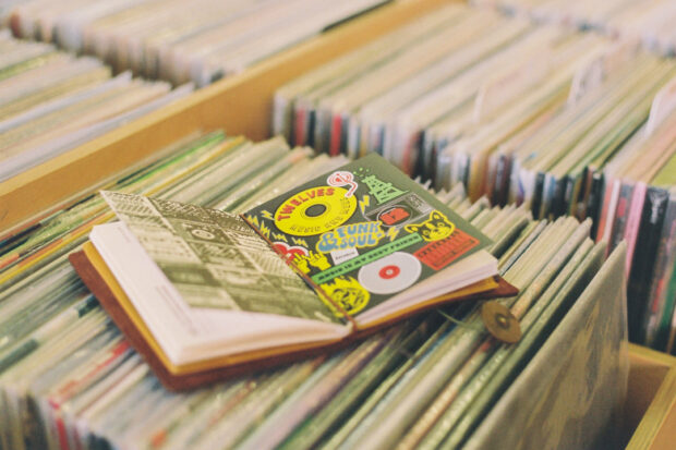 A notebook with colorful stickers and drawings is open on top of rows of vinyl records in a record store.