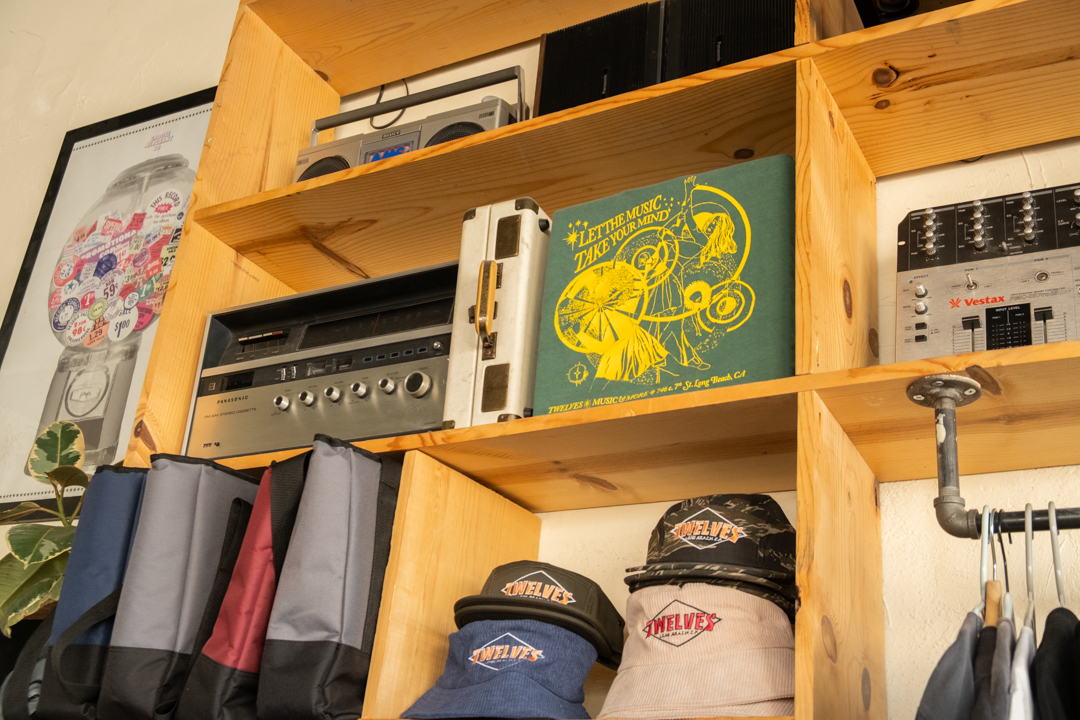 Wooden shelving containing TWELVES merchandise and other sound system machines and speakers.
