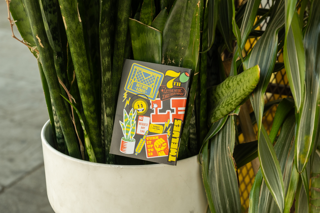 TRAVELERS’ notebook refill TWELVES RECORD Sticker (Passport Size) leaning against the store's iconic snake plant.
