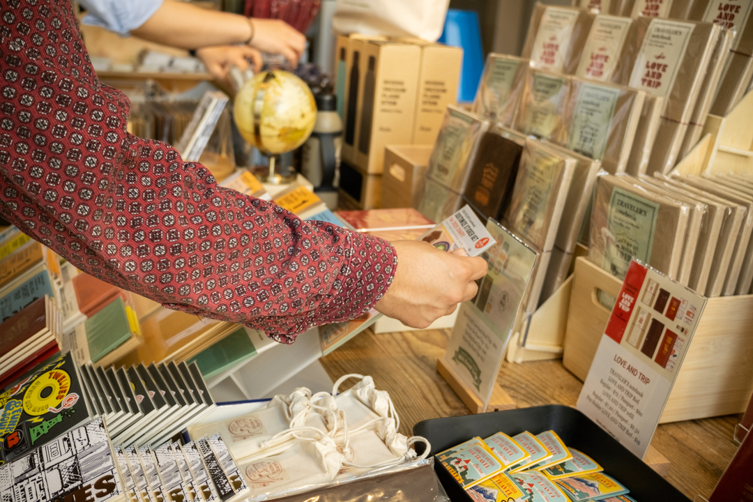 Shopper carefully selecting a notebook from the colorful array of TRAVELER'S journals and sticker sets.