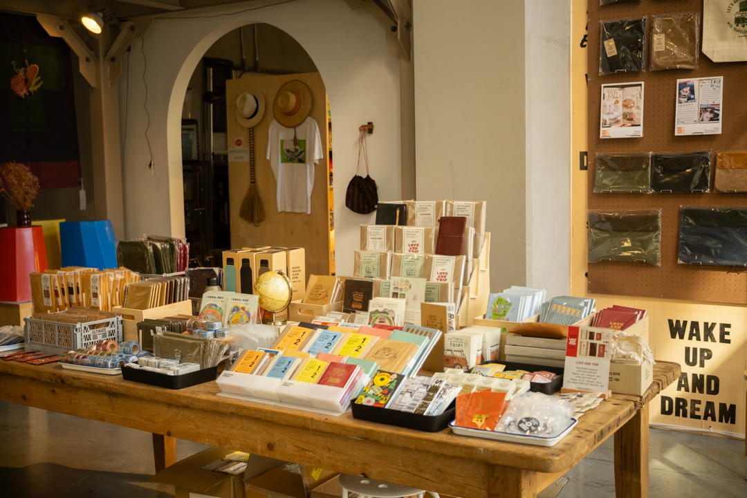 A closer view of the central product table displaying TRAVELER'S notebooks in various colors, masking tape, and travel-themed accessories.