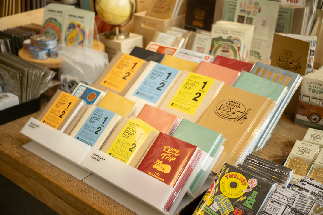 Vibrant display of TRAVELER'S notebooks featuring the "SHORT TRIP" series in yellow, blue, and coral alongside "LOVE AND TRIP" editions.