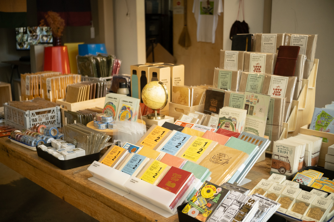 Beautifully arranged display of TRAVELER'S notebooks, Pan Am sticker sets, and other stationery goods bathed in warm natural light.