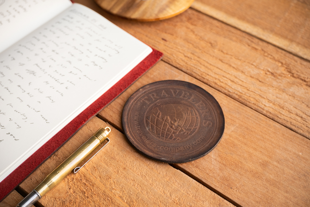 A worn TF Leather coaster next to a TRAVELER'S notebook.