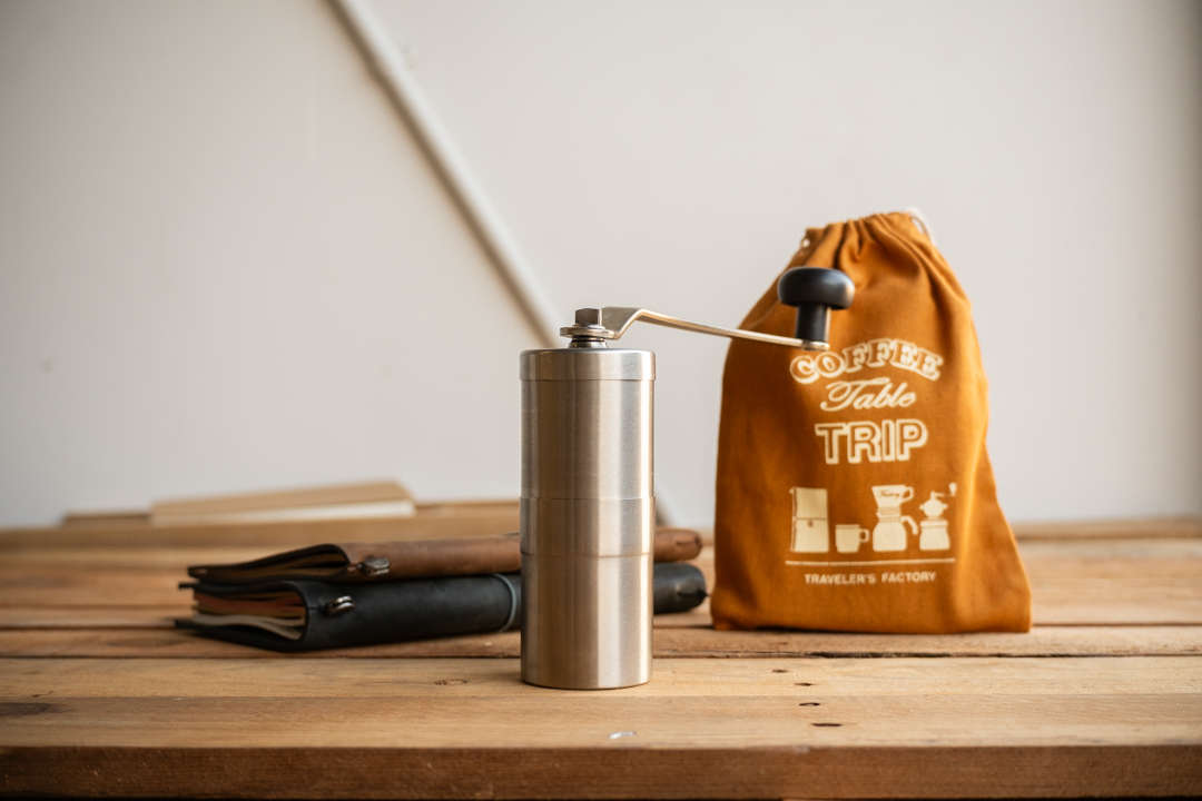 A coffee grinder on a table next to two TRAVELER'S notebook and coffee bag.