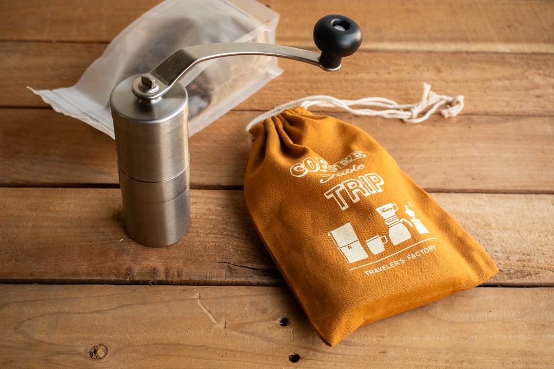 A light brown TF Original coffee bag next to a handheld coffee grinder.