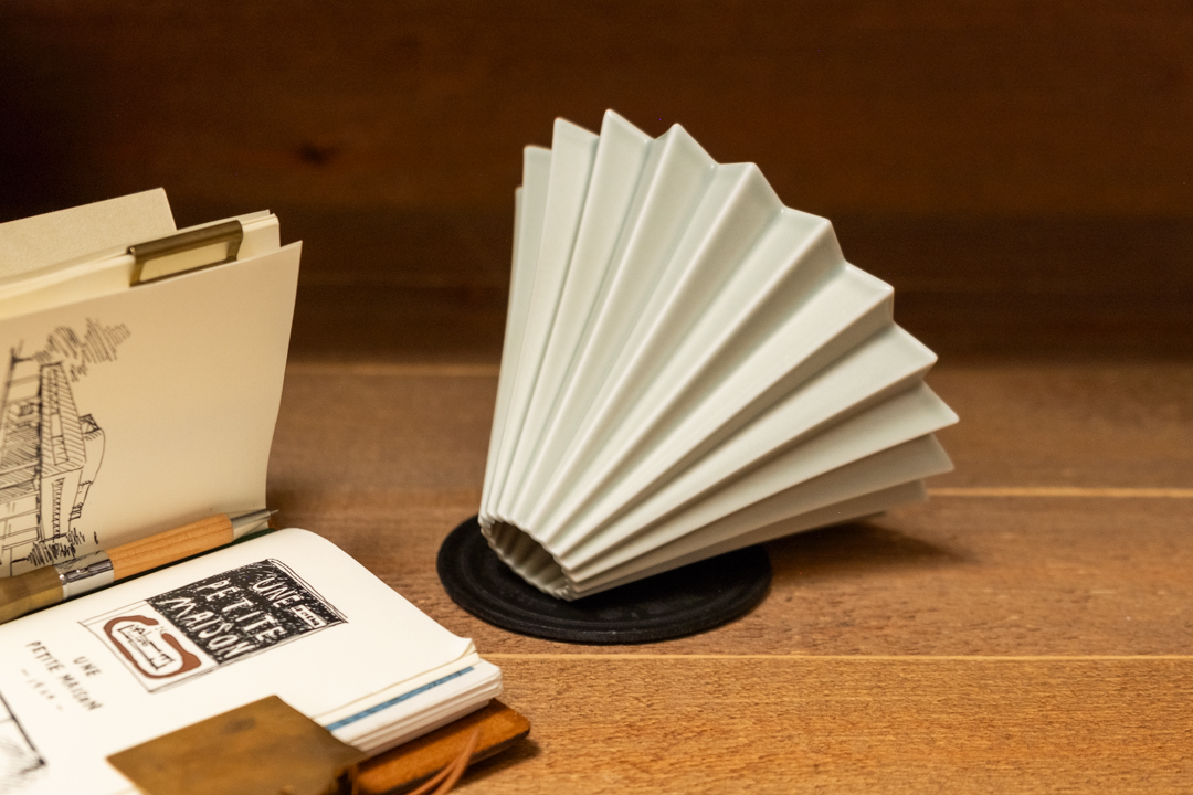 A gray ORIGAMI dripper next to a TRAVELER'S notebook in Passport Size.