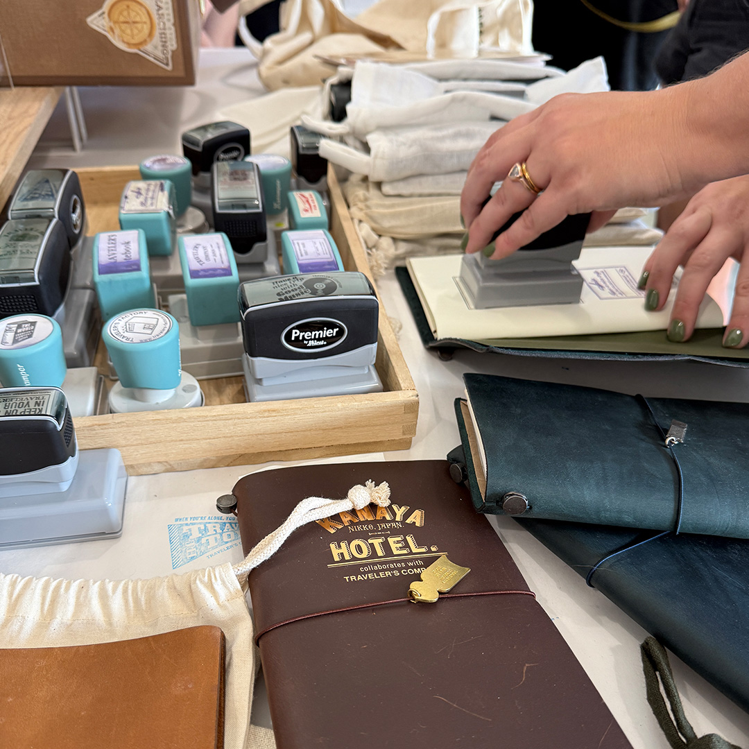 A user stamping their TRAVELER'S notebook with stamp caravan stamps.