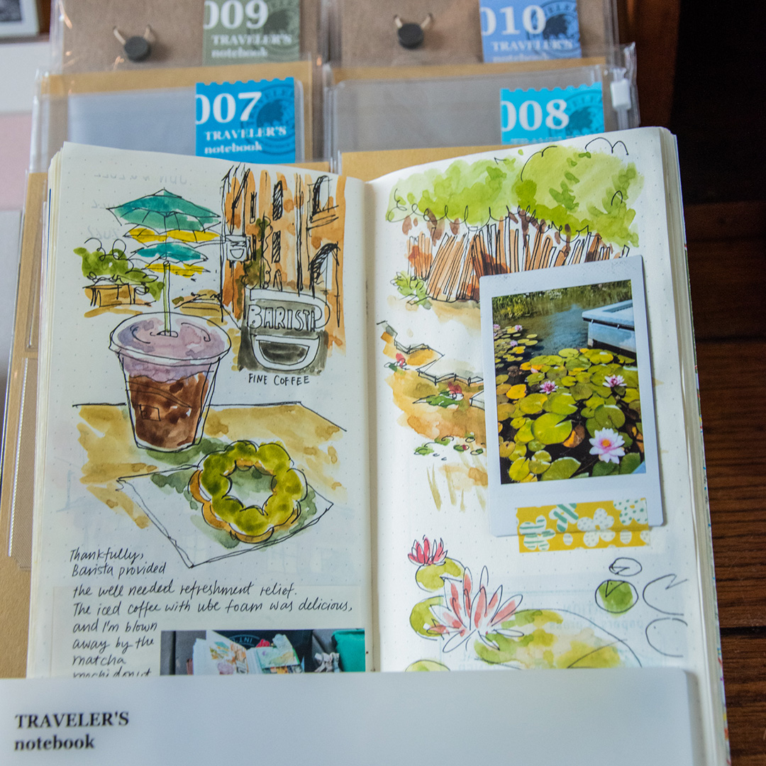 A TRAVELER'S notebook refill is opened to display the content of watercolor sketches, polaroid photo, and writing.