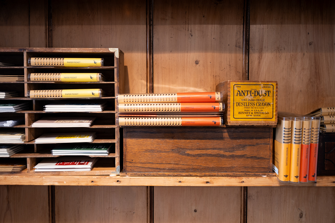 The TRAVELER'S COMPANY display inside the Paper and Grace stationery shop is filled with TRAVELER'S COMPANY items, such as TRAVELER'S notebooks, refills, and other paper goods and stationery, which are displayed on a vintage wooden shelf.