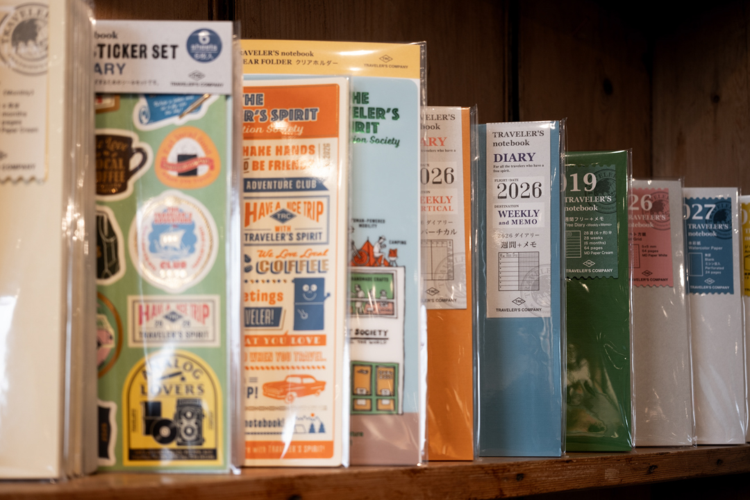 The TRAVELER'S COMPANY display inside the Paper and Grace stationery shop is filled with TRAVELER'S COMPANY items, such as TRAVELER'S notebooks, refills, and other paper goods and stationery, which are displayed on a vintage wooden shelf.