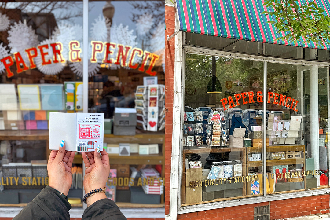 A person holding a TRAVELER'S notebook Passport Size insert outside of Paper & Pencil store, which features a brick facade, big windows, a sign-painted store name, and a multi-colored awning.