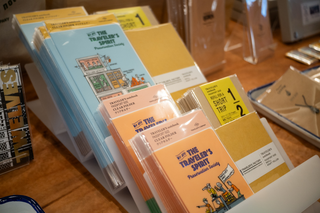 Notebooks and other stationery are standing on an acrylic on an exhibitor table filled with TRAVELER'S COMPANY items and products.
