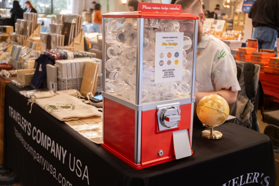 Capsule toy machine filled with pin buttons resting on the TRAVELER'S COMPANY USA table at the California pen show.