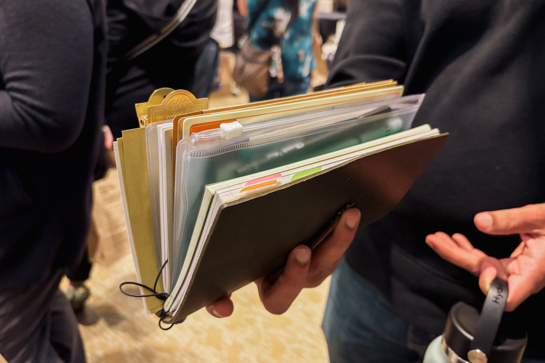 Person holding a TRAVELER'S notebook filled with notes and stationery.
