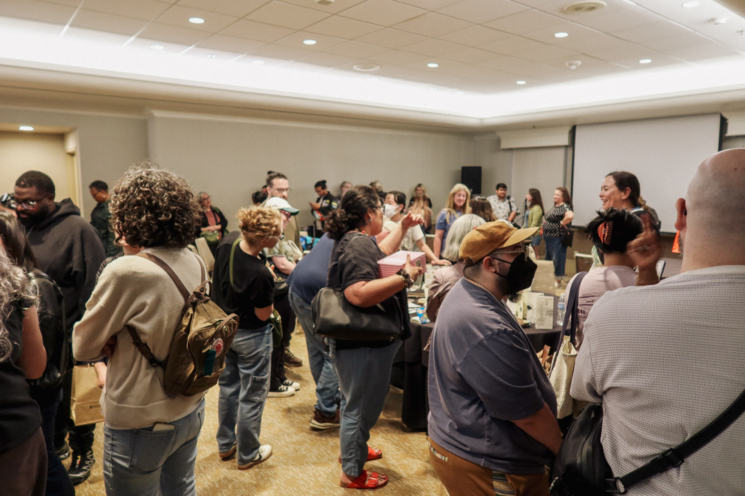 People are surrounding a round table, which is an exhibit of travel journals created by artists who use TRAVELER'S notebooks.
