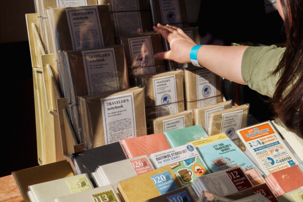 A close-up of the TRC USA table, which is filled with TRAVELER'S notebooks and a person is reaching for an item at the table.
