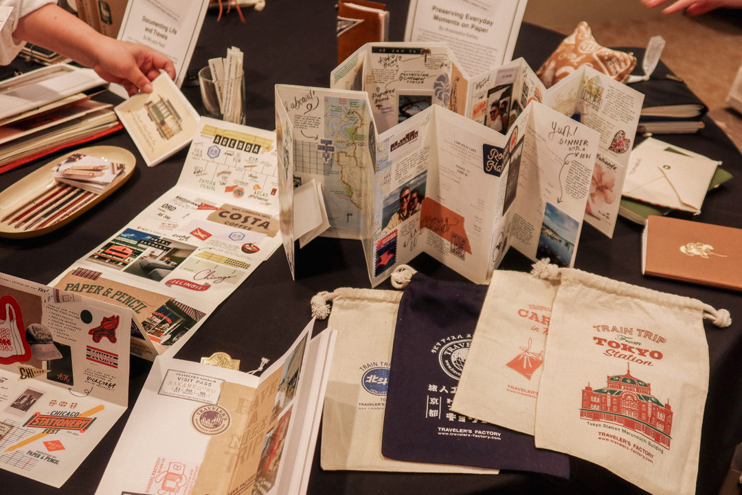 An exhibit of travel journals created by artists who use TRAVELER'S notebooks on a round table with black tablecloth.
