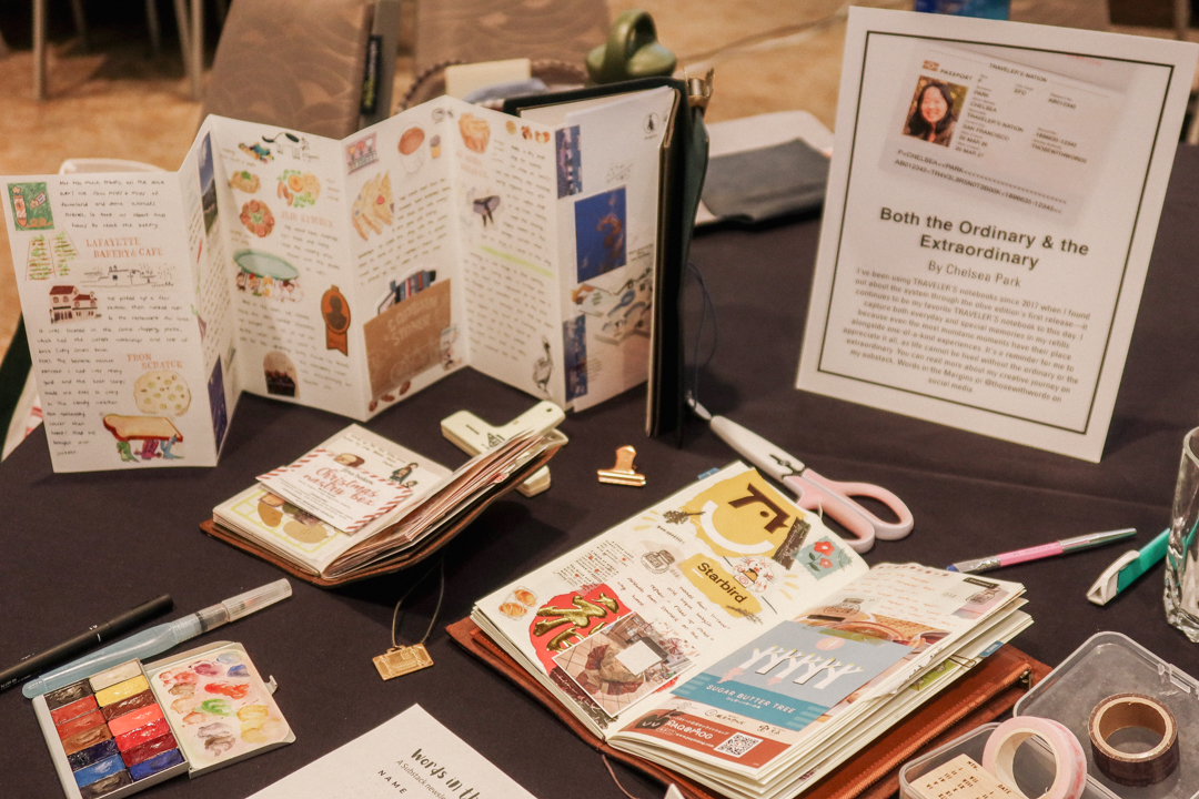 An exhibit of travel journals created by artists who use TRAVELER'S notebooks on a round table with black tablecloth.