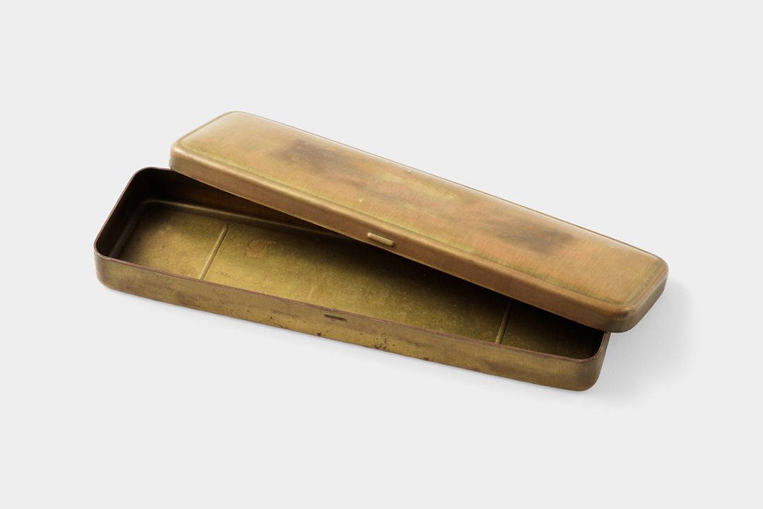 A used brass pen case that has a heavy patina due to the unfinished and uncoated solid brass, which has oxidized.