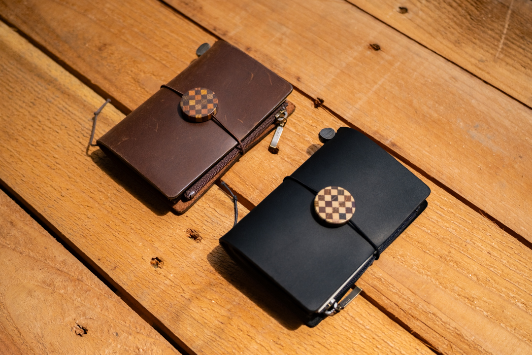 Black and brown TRAVELER'S notebooks in Card Size decorated with a YOSEGI wooden charm on a wooden table. 