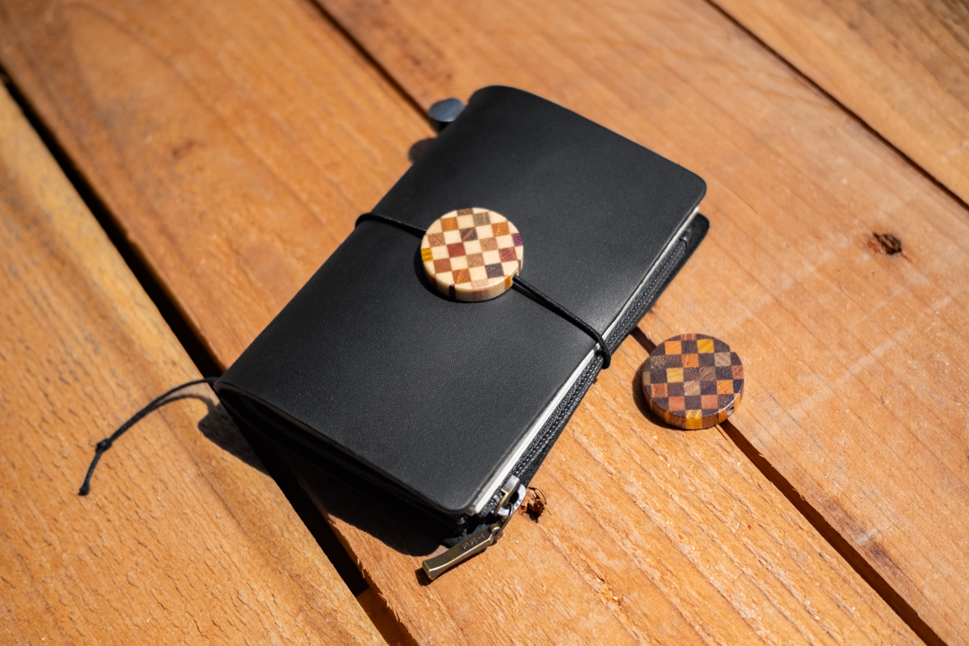 A black TRAVELER'S notebook Card Size decorated with a YOSEGI wooden charm on a wooden table. 