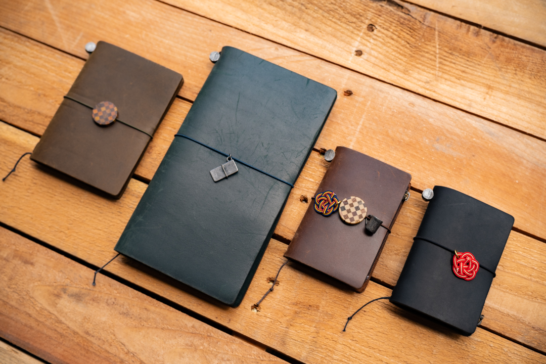 TRAVELER'S notebooks decorated with Tin, YOSEGI, and MIZUHIKI charms against a wooden table.