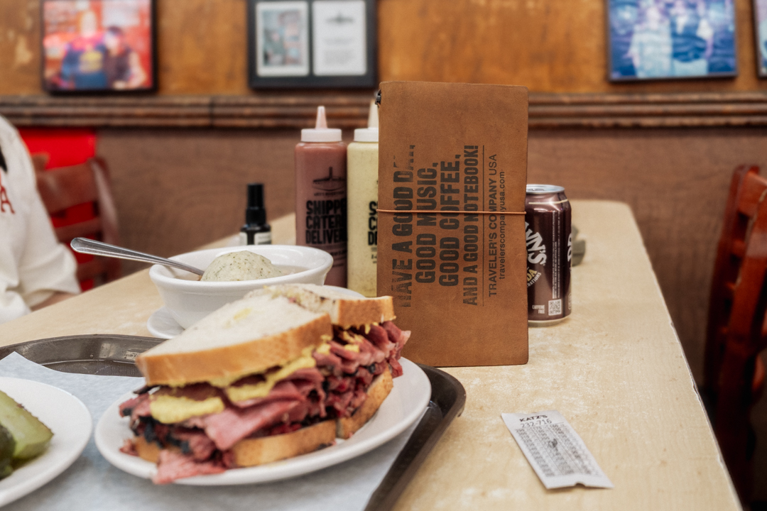 TRAVELER'S notebook positioned next to a pastrami sandwich.