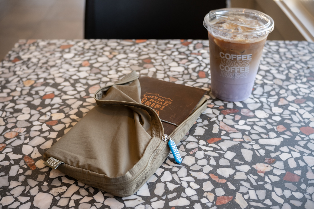 A TRAVELER'S notebook in an olive green TO&FRO Organizer in Regular Size beside an ube latte on a terrazzo table.