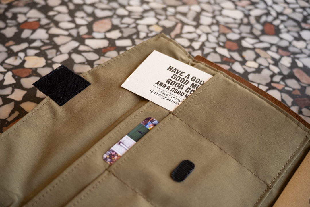 A TRAVELER'S notebook open to a TO&FRO Zipper pouch in olive green showing that it can hold credit cards and business cards.