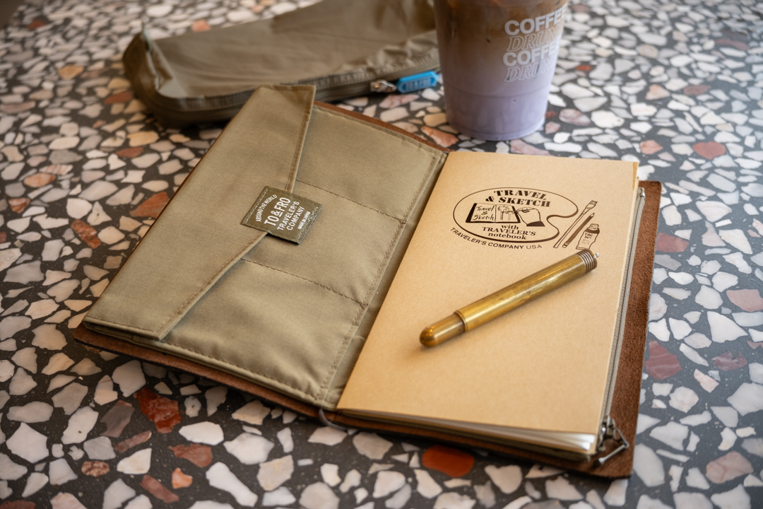 A TRAVELER'S notebook open to a TO&FRO Zipper pouch in olive green beside an ube latte and olive green TO&FRO Organizer in Regular Size.