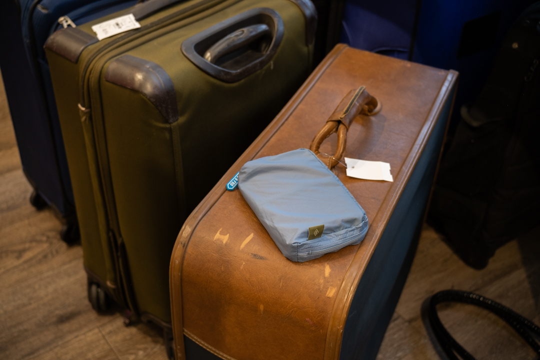 A TO&FRO organizer in blue protecting a passport size TRAVELER'S notebook, resting on a vintage leather luggage.