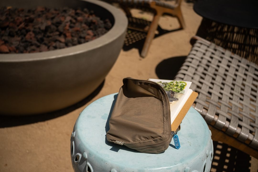 A finished painting in Spiral Ring Notebook stored in a TO&FRO zip organizer, on a small outdoor table on a patio.