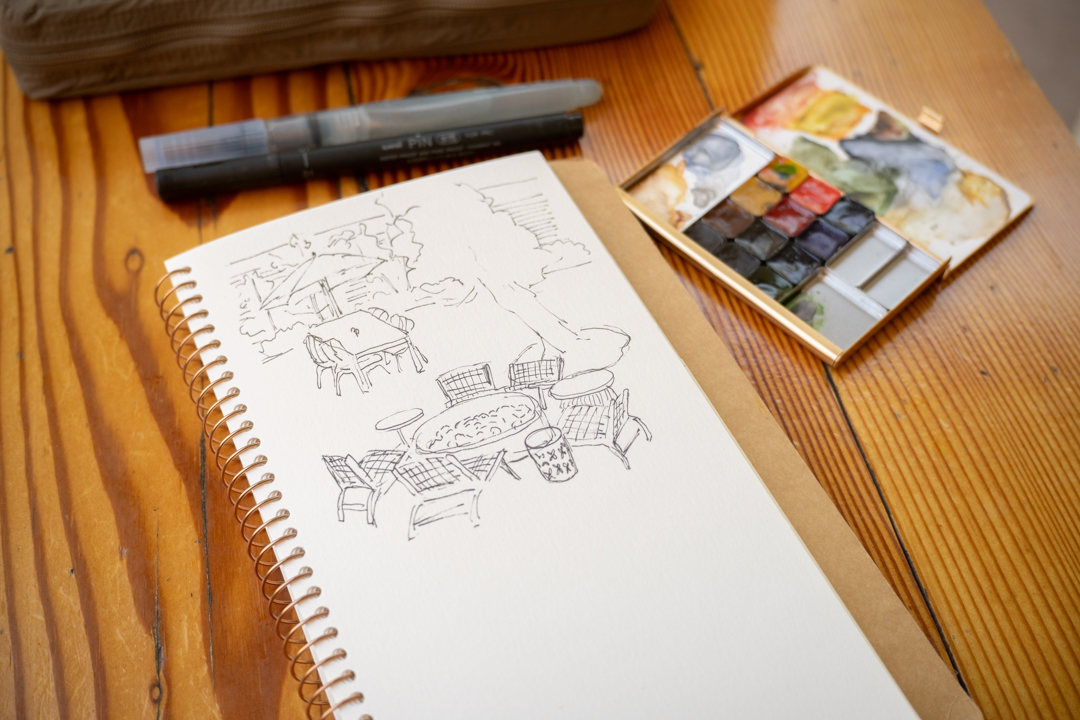 A sketch of the outdoor patio in a spiral ring notebook which is propped up a a chair and restaurant table.
