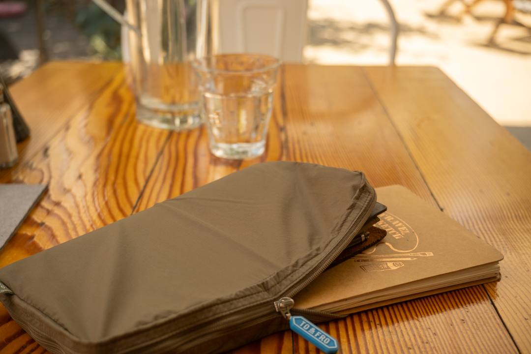 A wooden restaurant table with a TO&FRO organizer protecting the TRAVELER'S notebook.