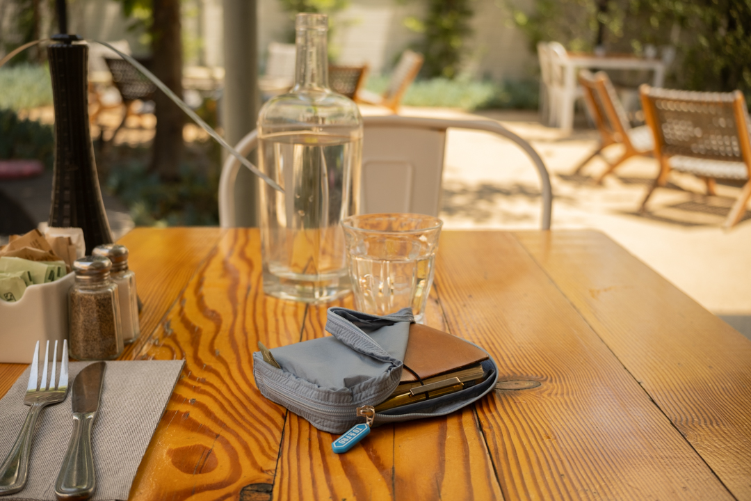 A wooden restaurant table with a TO&FRO organizer protecting the TRAVELER'S notebook.