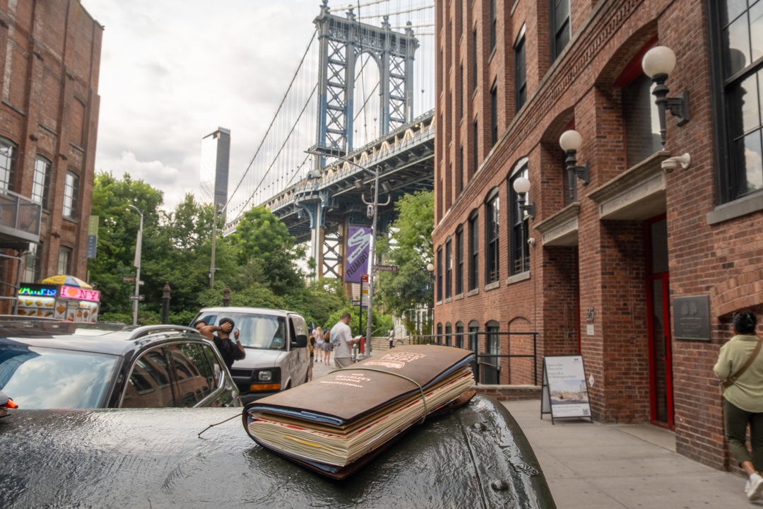 A view of the Manhattan Bridge from Dumbo, Brooklyn, with a TRAVELER'S notebook resting on a mailbox in the foreground.