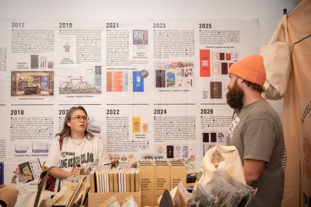 TRAVELER'S COMPANY USA staff chats with a customer by the 20-year History Guide wall.