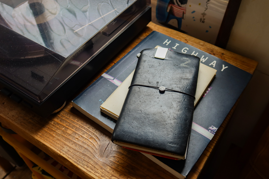 A black TRAVELER'S notebook resting on a book next to a record player.