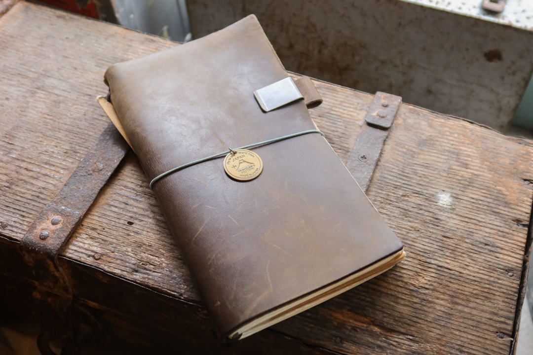 An Olive TRAVELER'S notebook with a patina resting on a wooden crate.