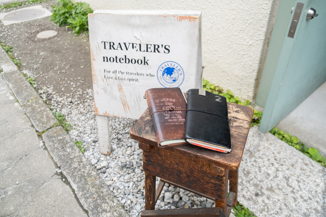 Two TRAVELER'S notebooks resting on a wooden stool outside of TRAVELER'S FACTORY Nakameguro.
