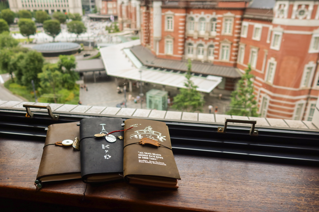 3 TRAVELER'S notebooks resting in front of a window which look out to the exterior of TOKYO Station.
